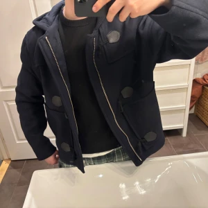 Mörkblå duffeljacka från Zara - Säljer en snygg mörkblå duffeljacka från Zara med huva och dragkedja och Jackan har unika knapplösningar och två stora fickor framtill. Perfekt för våren!