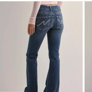 Blå bootcut jeans nelly - Snygga blå bootcut jeans med klassisk femficksdesign och dekorativa sömmar på bakfickorna. Perfekta för en avslappnad stil med en touch av retro.                                  Storlek 32🩷
