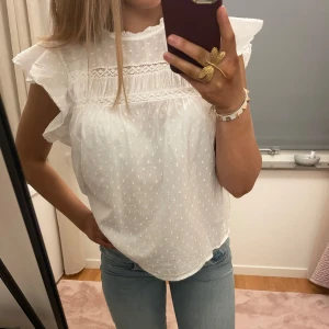 Vit blus med volangdetaljer - Säljer en söt vit blus med volangdetaljer och spets. Blusen har korta ärmar och ett diskret pprickigt mönster. Perfekt för varma sommardagar☀️. Storlek S men passar även M💕 priset kan diskuteras och tveka inte att höra av dig vid frågor❤️