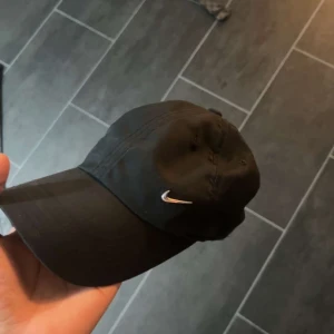 Svart keps med logotyp - Snygg svart keps med en liten broderad logotyp på sidan. Perfekt för en casual look och skydd mot solen. Justerbar passform för bekvämlighet.