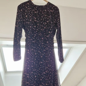 Svart klänning med prickigt mönster - Snygg svart klänning med ljusa prickar och långa ärmar. Perfekt för en stilren look. Klänningen har en elegant passform och är idealisk för både vardag och fest.