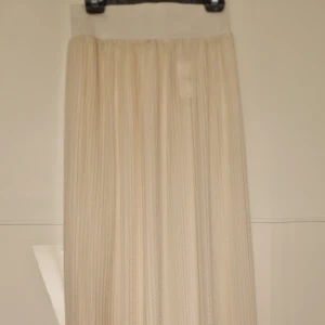 Vit långkjol - Elegant vit långkjol med plisserad design. Perfekt för en stilren och sofistikerad look. Kjolen har en mjuk och flödande passform som ger en vacker siluett.