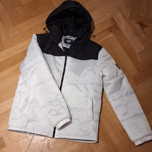 Vit och svart jacka från Denim Project - Säljer en snygg vit och svart jacka från Denim Project i storlek XL. Jackan har en dragkedja framtill och en huva för extra skydd. Perfekt för kyligare dagar med sin stilrena design.
