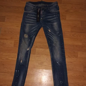 Blå jeans med slitningar och dragkedja - Snygga blå jeans med coola slitningar och en unik dragkedja framtill. De har en modern look med blekta detaljer och stänk för en edgy stil. Perfekta för dig som vill sticka ut!
