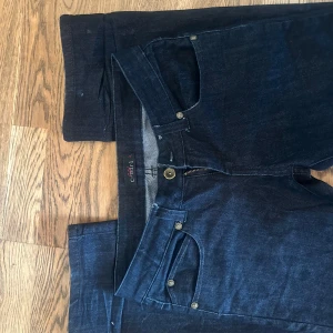 Mörkblå jeans med mönster på ena fickan - Snygga mörkblå jeans med en unik dekoration på bakfickan. 