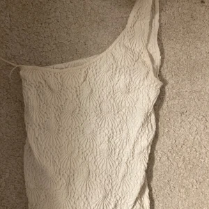 Vit oneshoulder topp - Säljer en stilren vit oneshoulder topp med ett unikt texturerat mönster. Perfekt för en trendig look. Passar bra till både jeans och kjol.