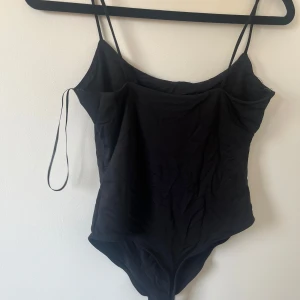 Svart body med tunna axelband - Elegant svart body med tunna axelband och enkel design. Perfekt för en stilren look. Använd max 1 gång 