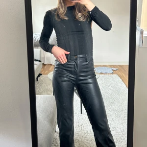Svarta skinnbyxor - Snygga svarta skinnbyxor med hög midja och raka ben . Byxorna har en klassisk design med dragkedja och knapp framtill. Perfekta för en stilren look.