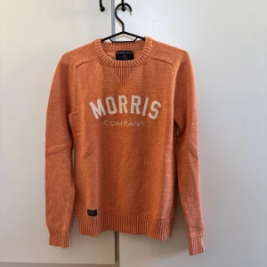 Orange tröja från Morris - Säljer en snygg orange tröja från Morris med texten 'Morris Company' på bröstet. Tröjan har långa ärmar och ribbade muddar vid ärmslut och nederkant. Perfekt för en stilren look.