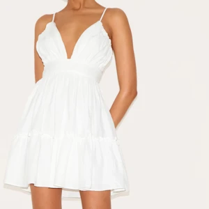 Vit kortklänning med volangdetaljer - Säljer en söt vit kortklänning med smala axelband och volangdetaljer. Klänningen har en djup v-ringning och en luftig passform, perfekt för student eller midsommar 💌