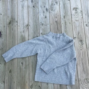 Grå stickad tröja från Lindex - Mysig grå stickad tröja från Lindex för barn. Tröjan har en enkel design med ribbade detaljer vid ärmslut och nederkant. Perfekt för kyligare dagar.