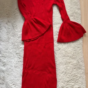 Röd klänning från Gina Tricot - Snygg röd klänning från Gina Tricot med  ärmar och volangdetaljer vid ärmsluten. Klänningen är ribbad och har en figurnära passform som ger en elegant look. Perfekt för att sticka ut med sin klara färg och stilrena design.