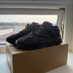 Adidas Yeezy Boost 700 - Säljer ett par svarta Adidas Yeezy Boost 700 sneakers. Skorna har en chunky design med snörning och är tillverkade i en kombination av material för en stilren look. Perfekta för dig som vill ha en trendig och bekväm sneaker. Tyget på insidan av skon vid hälen har slitits upp.