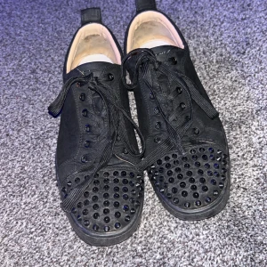 Svarta sneakers med nitar - Snygga svarta sneakers med nitar på tån och röda sulor. Skorna har snörning och en stilren design som passar perfekt för en edgy look. Äkta skor, men sulan är lite sliten där med priset. Kan också diskutera priset👍