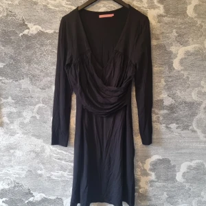 Svart klänning från Pernilla Wahlgren Collection - Snygg svart jerseyklänning från Pernilla Wahlgren Collection. Klänningen har en v-ringad design och långa ärmar, perfekt för en stilren look. Materialet är mjukt och stretchigt med 92% viskos och 8% elastan.