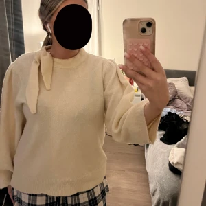Beige tröja med knyt - Säljer en mysig beige tröja med en unik knytdetalj vid halsen. Tröjan har långa ärmar och en avslappnad passform, perfekt för kyligare dagar. Passar bra till både jeans och kjol.