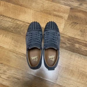 Grå sneakers med nitar från Christian Louboutin - Snygga grå sneakers från Christian Louboutin med coola nitar på ovansidan. Skorna har en klassisk snörning och den ikoniska röda sulan. Perfekta för att ge din outfit en edgy touch. Lite färgtapp på några spikar men det är inget som syns allt för mycket och skorna är storlek 41 men dom passar också 42, pris kan diskuteras vid snabb affär, box, kvitto och dustbag medföljer