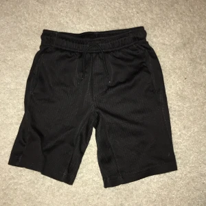 Svarta träningsshorts från SOC - Säljer ett par svarta träningsshorts från SOC. De har en bekväm passform med snörning i midjan och är tillverkade i ett lätt och andningsbart material. Perfekta för sport och träning.