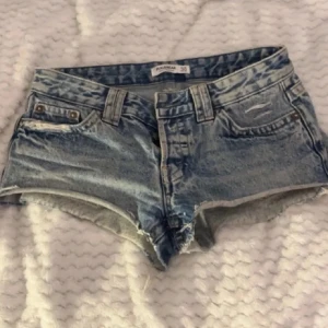 Blå jeansshorts från PacSun - Snygga blå jeansshorts från pull & bear med fransiga kanter och klassisk femficksdesign. Perfekta för en avslappnad sommarlook. De har en lågmidjad passform och är tillverkade i slitstarkt denim.