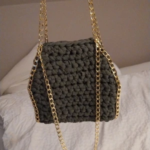 Khakigrön virkad väska med guldkedja - Snygg khakigrön virkad väska med en elegant guldkedja. Perfekt för att ge din outfit en unik touch. Väskan har en modern och trendig design som passar perfekt för olika tillfällen.