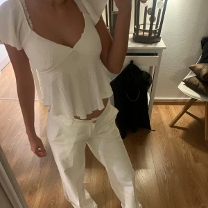 Vit blus med volangdetaljer - Säljer en söt vit blus med volangdetaljer och v-ringning. Blusen har korta ärmar och en luftig passform, perfekt för varma dagar. Den är gjord i ett lätt och bekvämt material som ger en fin struktur. Knappast använd❤️❤️