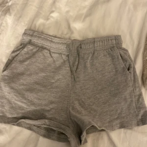 Grå shorts  - Säljer ett par grå shorts med elastisk midja och snörning. Perfekta för en avslappnad stil. De har en bekväm passform och är gjorda i ett mjukt material.