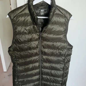 Olivgrön dunväst från Uniqlo - Säljer en olivgrön dunväst från Uniqlo. Västen är ultralätt och har en dragkedja framtill. Perfekt inför våren.