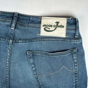 Blå jeans från Jacob Cohen - Snygga blå jeans från Jacob Cohen med klassisk femficksdesign och knappgylf. Jeansen har en stilren look med subtila detaljer och en broderad logga på myntfickan som är i perfekt skick! Alla Jacob Cohën jeans är 34" längd. W34. 