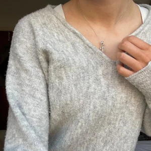 Grå stickad tröja  - Mysig grå stickad tröja med v-ringad hals. Perfekt för kyligare dagar med sin mjuka och bekväma passform. Tröjan har långa ärmar och en avslappnad stil som passar till det mesta.