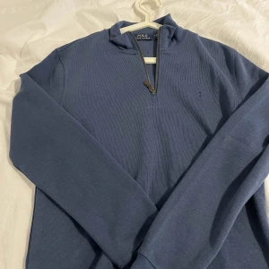 Blå tröja från Polo Ralph Lauren - Snygg blå tröja från Polo Ralph Lauren med dragkedja vid halsen. Tröjan har långa ärmar och en diskret ribbad struktur. Perfekt för en stilren och avslappnad look. Helt ny inga defekter. Storlek M men passar mer som S/M