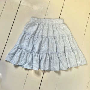 Ljusblå kjol - Söt ljusblå kjol med blommigt mönster och volanger! Kjolen är skön och luftig och slutar strax över knäna. Kjolen är i storlek S men har en elastisk midja så passar egentligen till minst en storlek uppåt 🩵