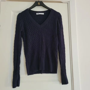 Mörkblå tröja från Zara - Säljer en mörkblå tröja från Zara med ett snyggt kabelstickat mönster. Tröjan har en v-ringad hals och långa ärmar. Den är både stilren och bekväm.