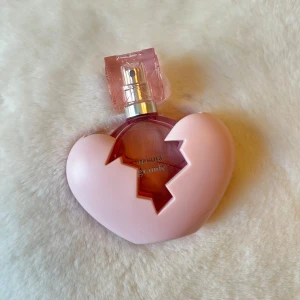 Parfym i hjärtformad flaska - Säljer en unik parfym från Ariana Grande i en hjärtformad flaska med rosa detaljer. Flaskan har en kreativ design med ett sprucket hjärta och en rosa spraykork. Perfekt för den som älskar sötare doft och design!