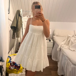 Vit  klänning - Säljer en söt vit klänning med smala axelband och volangdetaljer. Perfekt för sommardagar med sin luftiga design och sköna passform. Klänningen har en smockad överdel som ger en fin siluett.