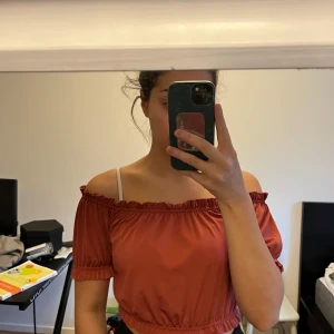 Rostfärgad offshoulder topp - Säljer en snygg rostfärgad offshoulder topp med korta ärmar och elastiska kanter. Toppen är croppad och har en luftig passform, perfekt för varma dagar.