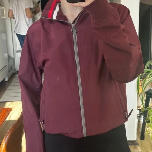 Vinröd jacka från Timberland - Säljer en snygg vinröd jacka från Timberland med dragkedja framtill. Jackan har långa ärmar och en stilren design. Perfekt för höst och vår med sin bekväma passform och klassiska look.