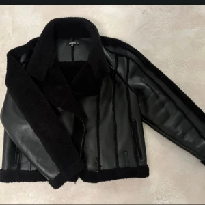 Svart skinnjacka med pälsdetaljer - Snygg svart skinnjacka med mjuka pälsdetaljer på krage, ärmslut och nederkant. Jackan har en klassisk design med en modern twist och är perfekt för kyligare dagar. Den har en stilren look och passar bra till olika outfits.