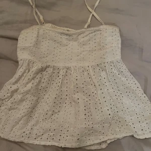 Vit ärmlös topp - Säljer en söt beige ärmlös topp med broderade detaljer och smala axelband. Toppen har ett luftigt och lätt material, perfekt för varma dagar. Den har en fin struktur med små hål som ger en unik look. Köp gärna med köp nu :)