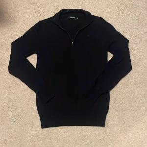 Svart tröja med dragkedja från J.Lindeberg - Snygg svart tröja från J.Lindeberg med halv dragkedja och diskret broderad logga på bröstet. Perfekt för en stilren look. Tröjan har långa ärmar och är tillverkad i ett mjukt material. Pris går att diskuteras.