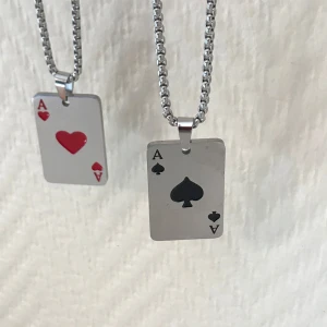 Halsband med spelkortshängen - Två coola halsband med spelkortshängen i form av ess. Ett hänge har ett rött hjärter ess och det andra ett svart spader ess. Kedjorna är i silverfärg och har en robust design.