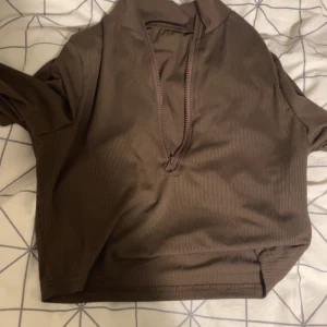 Brun ribbad tröja med dragkedja - Säljer en brun ribbad tröja med halv dragkedja framtill. Tröjan har en hög krage och långa ärmar.