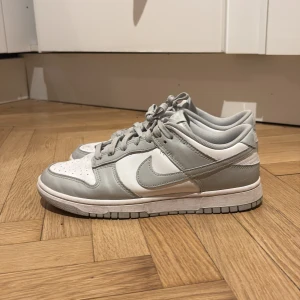 Nike Dunk i grått och vitt - Säljer ett par stilrena Nike Dunk sneakers i grått och vitt.  Nypris 1400kr. Knappt använda