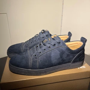 Mörkblå sneakers från Christian Louboutin - Snygga mörkblå sneakers i mocka från Christian Louboutin med den ikoniska röda sulan. Skorna har snörning och en stilren design som passar perfekt för en trendig look.