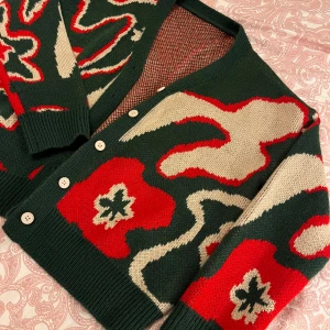 Mönstrad kofta i grönt och rött - Säljer en unik kofta med abstrakt mönster i grönt, rött och beige. Koftan har långa ärmar och knäpps med vita knappar framtill. Perfekt för att liva upp garderoben!