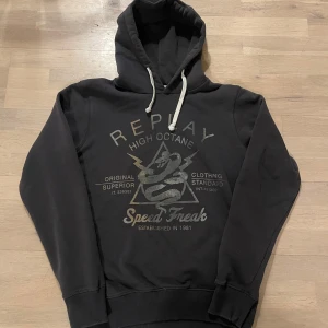 Replay hoodie - Säljer denna extremt snygga replay hoodie i mörkgrått/svart. Hoodien har en snygg design på magen samt snygga detaljer såsom snörena samt deras klassiska logga vid höften. Storlek L passar mer M. Hoodien är i perfekt skick, hör av er vid eventuella frågor!