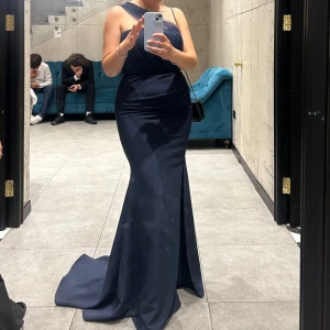 Marinblå långklänning med slits - Elegant marinblå långklänning med en stilren oneshoulder-design och en smickrande slits framtill. Perfekt för en kväll ute eller en speciell tillställning. Klänningen har en figurnära passform som framhäver silhuetten. Endast använd en gång, stl 38 🥰