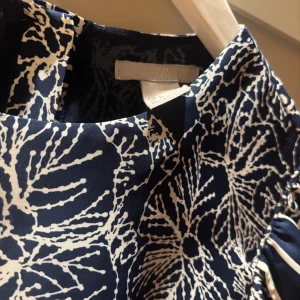 Blå och vit mönstrad klänning från H&M - Snygg blå klänning med vitt blommönster från H&M. Den har korta puffärmar och en rund halsringning. Perfekt för en somrig look! Storlek 34/ xs