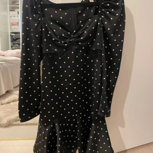 Svart prickig klänning från H&M - Snygg svart klänning med vita prickar från H&M. Klänningen har långa ärmar och en volangdetalj längst ner