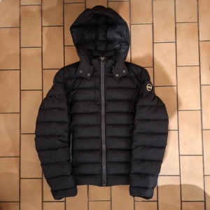 Colmar jacka - Säljer en snygg svart dunjacka från Colmar med huva, jackan är lite tunnare så perfekt nu till våren. Jackan är i fint skick förutom ett litet igensytt hål på ärmen( cirka 1 cm ) syns verkligen inte. Skriv om andra frågor, priset är inte hugget i sten!