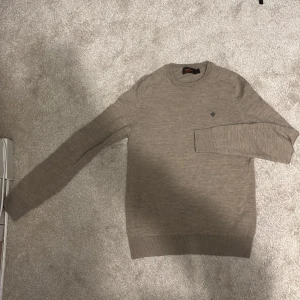 Beige stickad tröja från Morris - Säljer en stilren beige stickad tröja från Morris med ett diskret broderat emblem på bröstet. Tröjan har långa ärmar och ribbade muddar vid ärmslut och nederkant. Perfekt för en avslappnad men ändå elegant look. Nypris på denna är runt 1600kr. Skriv vid funderingar!🙌